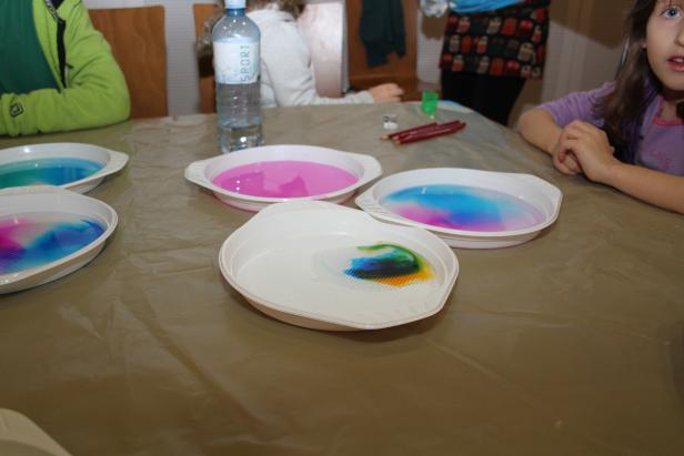 Kinder experimentieren mit farbigem Wasser in flachen Schalen auf einem Tisch.