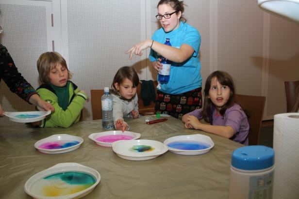 Kinder experimentieren mit Farben in Schüsseln an einem Tisch.