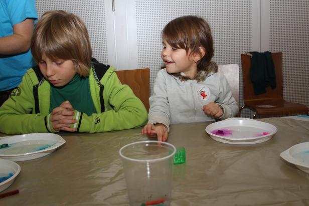 Zwei Kinder sitzen an einem Tisch und experimentieren mit Wasser und Farben.
