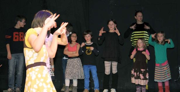Eine Gruppe Kinder steht auf einer Bühne und führt ein Theaterstück auf.