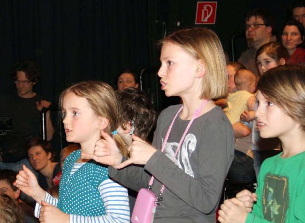 Eine Gruppe von Kindern macht Handzeichen vor einem Publikum.