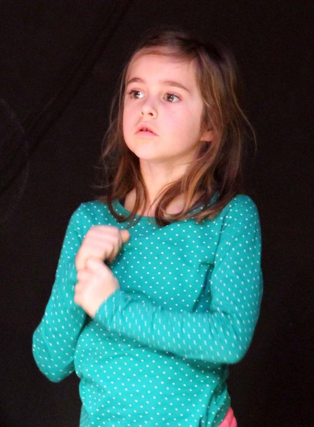 Ein junges Mädchen im gepunkteten Oberteil blickt erwartungsvoll nach oben.