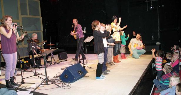 Eine Band spielt vor einem Publikum aus Kindern auf einer Bühne.