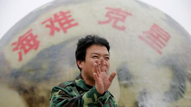 Ein Mann in Militärkleidung steht vor einer Kugel mit chinesischen Schriftzeichen.