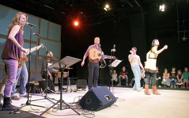 Eine Band spielt auf einer Bühne vor einem sitzenden Publikum.