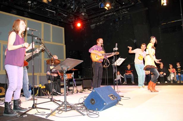 Eine Band spielt auf einer Bühne, während zwei Tänzer vor einem sitzenden Publikum auftreten.