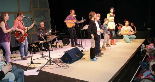 Eine Band spielt auf einer Bühne vor einem Publikum aus Kindern.