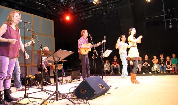 Eine Band spielt auf einer Bühne vor einem Publikum aus Kindern.