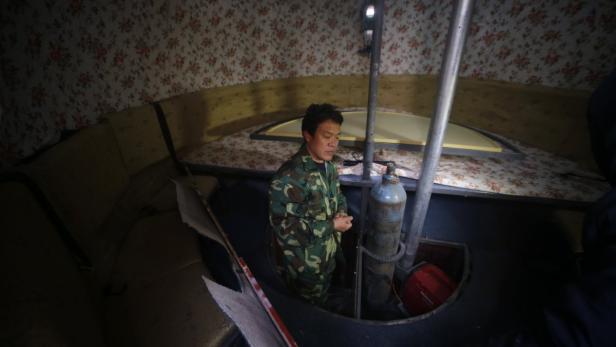 Ein Mann in Militärkleidung steht in einem kleinen Raum mit floral gemusterten Wänden.