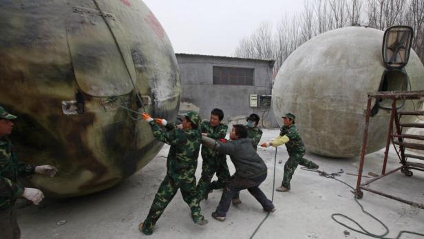Mehrere Personen ziehen an Seilen, die an zwei kugelförmigen Strukturen befestigt sind.