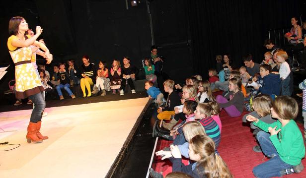 Eine Frau tritt vor einer Gruppe von Kindern auf einer Bühne auf.