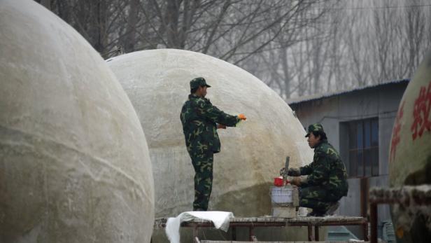 Zwei Arbeiter in Tarnkleidung bearbeiten große, kuppelförmige Objekte im Freien.