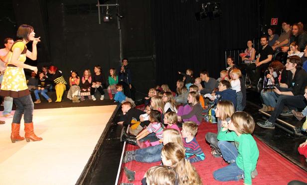Eine Frau steht auf einer Bühne vor einem Publikum aus Kindern und Erwachsenen.