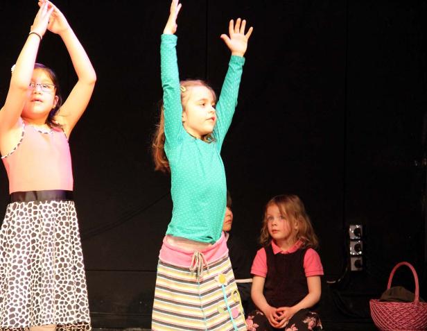 Mehrere Mädchen stehen auf einer Bühne und führen ein Theaterstück auf.