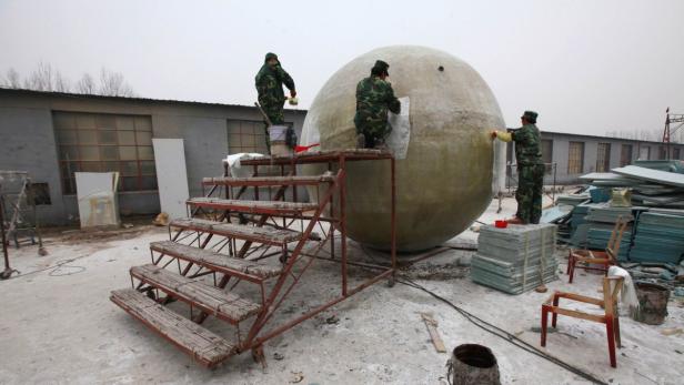 Drei Arbeiter in Tarnkleidung bearbeiten eine große Kugel im Freien.
