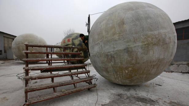 Ein Mann inspiziert eine der drei großen, kugelförmigen Kapseln auf einem Hof.
