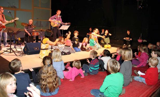 Eine Band spielt für eine Gruppe Kinder auf einer Bühne.