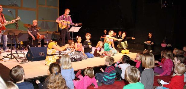 Eine Band spielt für eine Gruppe von Kindern auf einer Bühne.