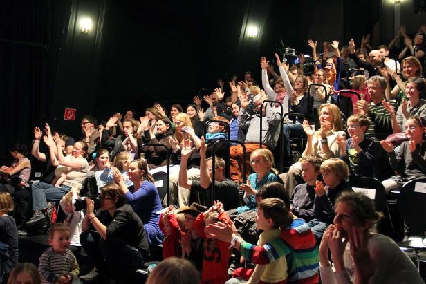 Ein Publikum applaudiert in einem dunklen Theater.