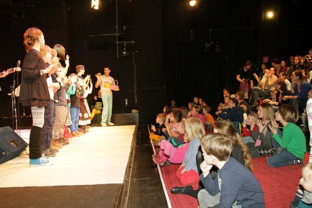 Eine Gruppe Kinder steht auf einer Bühne vor einem Publikum.