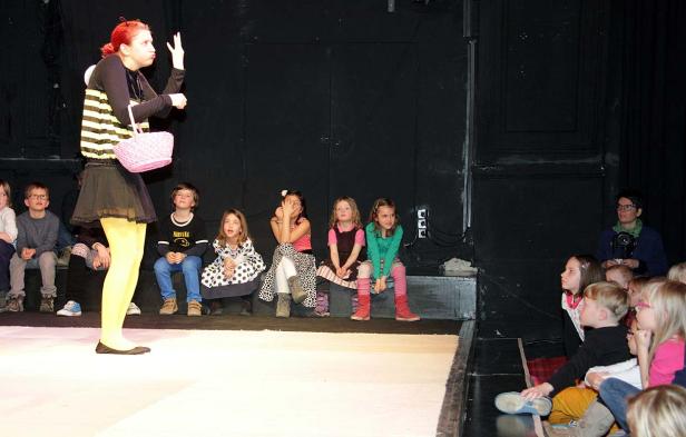 Eine Frau in einem Kostüm steht vor einer Gruppe von Kindern auf einer Bühne.