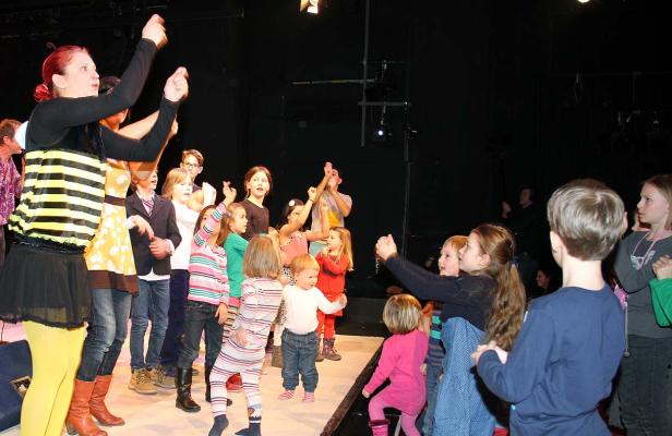 Eine Gruppe von Kindern steht auf einer Bühne, einige mit erhobenen Armen.