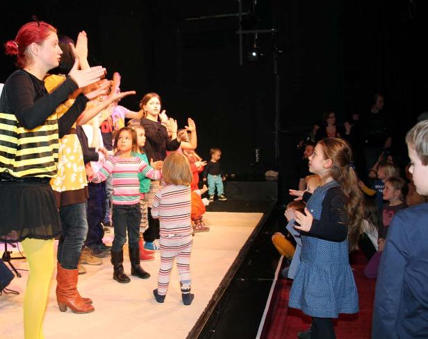 Eine Gruppe Kinder steht auf einer Bühne und klatscht in die Hände.