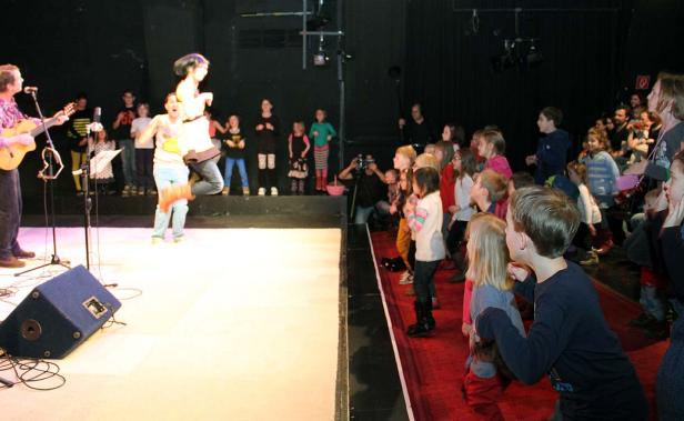 Eine Band spielt vor einem Publikum aus Kindern auf einer Bühne.