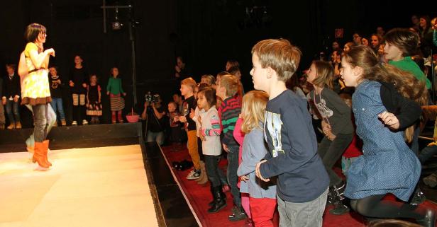 Eine junge Frau führt auf einer Bühne vor einer Gruppe von Kindern eine Performance auf.