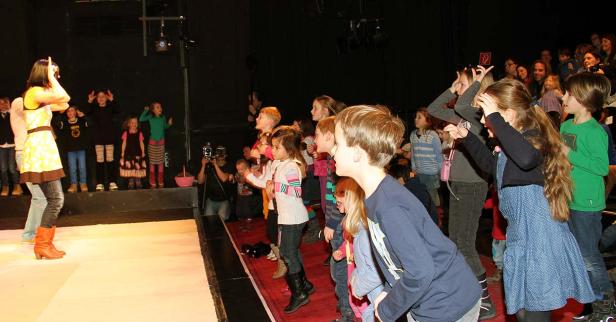 Eine Gruppe Kinder ahmt auf einer Bühne mit einer Frau Gesten nach.