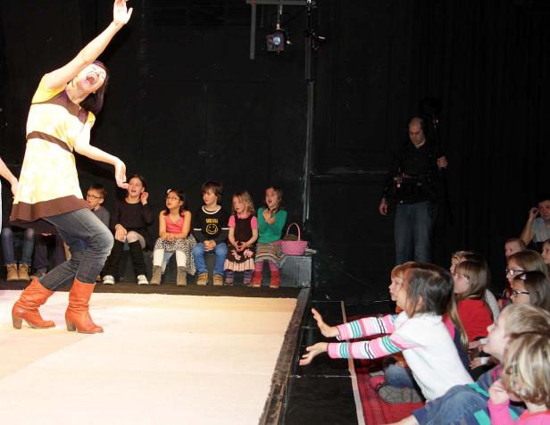 Eine Frau in Stiefeln führt eine Theatervorstellung für eine Gruppe Kinder auf.
