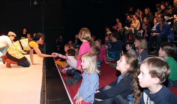 Eine Frau auf der Bühne interagiert mit einer Gruppe von Kindern im Publikum.