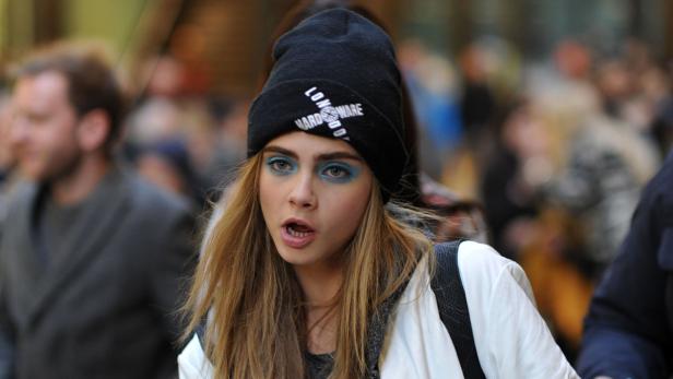 Cara Delevingne mit blauem Lidschatten und einer schwarzen Mütze in einer Menschenmenge.