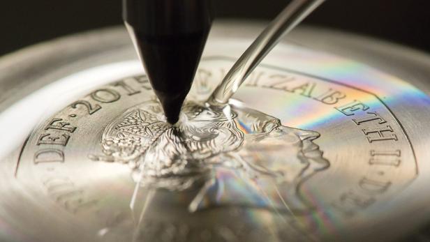 Eine Münze mit dem Abbild von Königin Elizabeth II. wird mit einem Werkzeug bearbeitet.