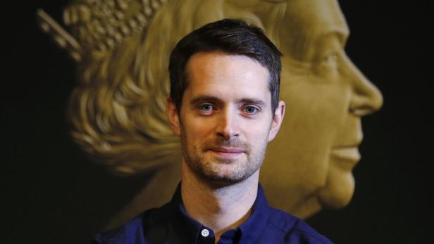 Ein Mann steht vor einem goldenen Porträt von Königin Elisabeth II..