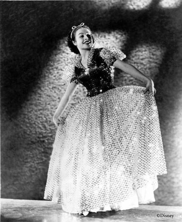 Eine Frau in einem glitzernden Kleid, das an Schneewittchen erinnert, posiert lächelnd.