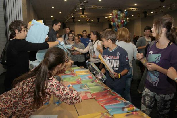 Eine Gruppe von Menschen steht an einem Tisch mit bunten Dokumenten und erhält Gegenstände.