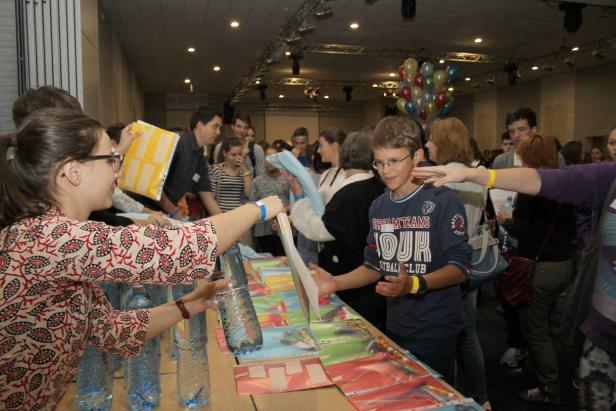 Ein Junge mit Brille steht an einem Tisch und nimmt ein Bild entgegen.