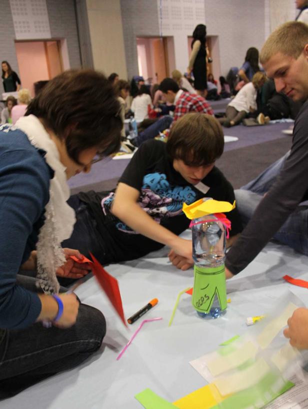 Eine Gruppe von Menschen sitzt auf dem Boden und bastelt mit Papier und einer Wasserflasche.