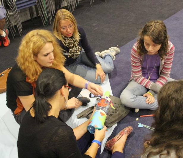 Eine Gruppe von Frauen und ein Mädchen sitzen auf dem Boden und basteln mit einer Plastikflasche.