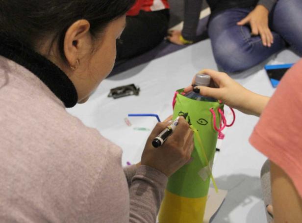 Eine Person bemalt eine mit Papier umwickelte Flasche, um ein Monster zu gestalten.