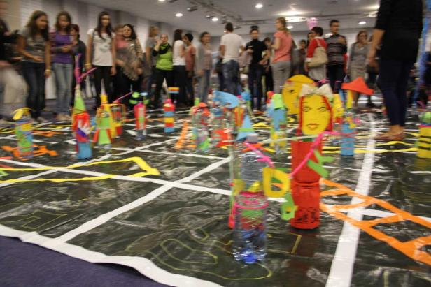 Eine Gruppe von Menschen betrachtet bunte, selbstgemachte Kunstobjekte auf dem Boden.