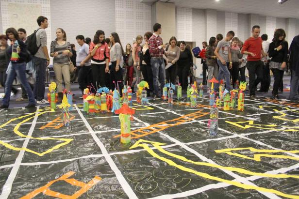 Eine Gruppe von Menschen steht um ein großes Spielfeld mit bunten Figuren herum.