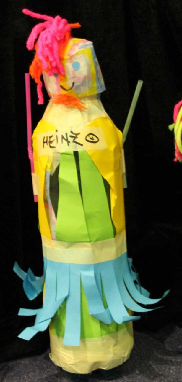 Eine bunte, selbstgemachte Figur mit dem Namen „Heinzo“ steht vor einem schwarzen Hintergrund.