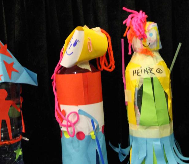 Selbstgebastelte Puppen aus Plastikflaschen und Papier vor schwarzem Hintergrund.