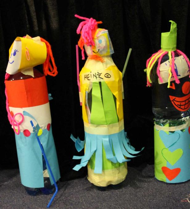 Drei bunte, selbstgemachte Figuren aus Plastikflaschen und Papier stehen nebeneinander.