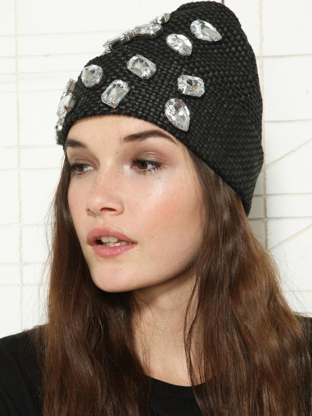 Eine Frau trägt eine schwarze Mütze, die mit großen, klaren Schmucksteinen verziert ist.