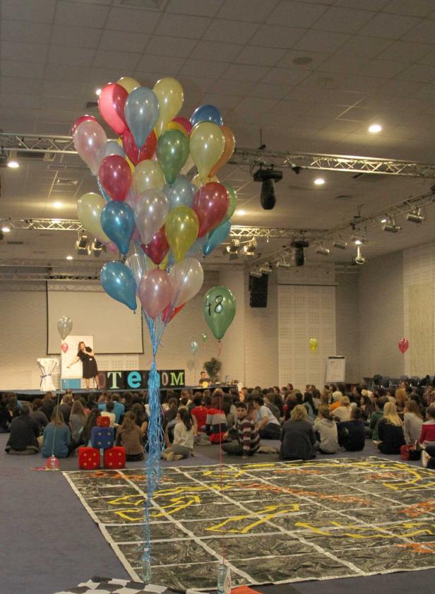 Eine Gruppe von Menschen sitzt auf dem Boden vor einer Bühne mit Ballons.