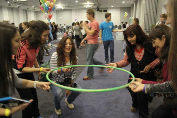 Eine Gruppe von Frauen spielt mit einem Hula-Hoop-Reifen in einem großen Raum.