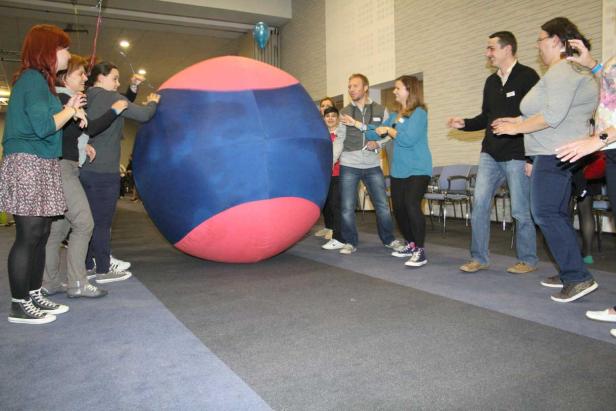 Eine Gruppe von Menschen spielt mit einem riesigen, rot-blauen Ball in einem Raum.